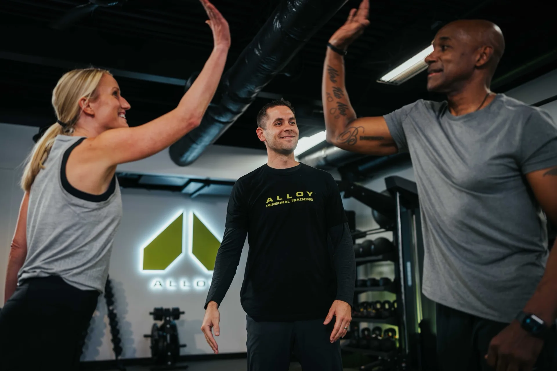Two clients high-fiving their smiling coach after finishing a set